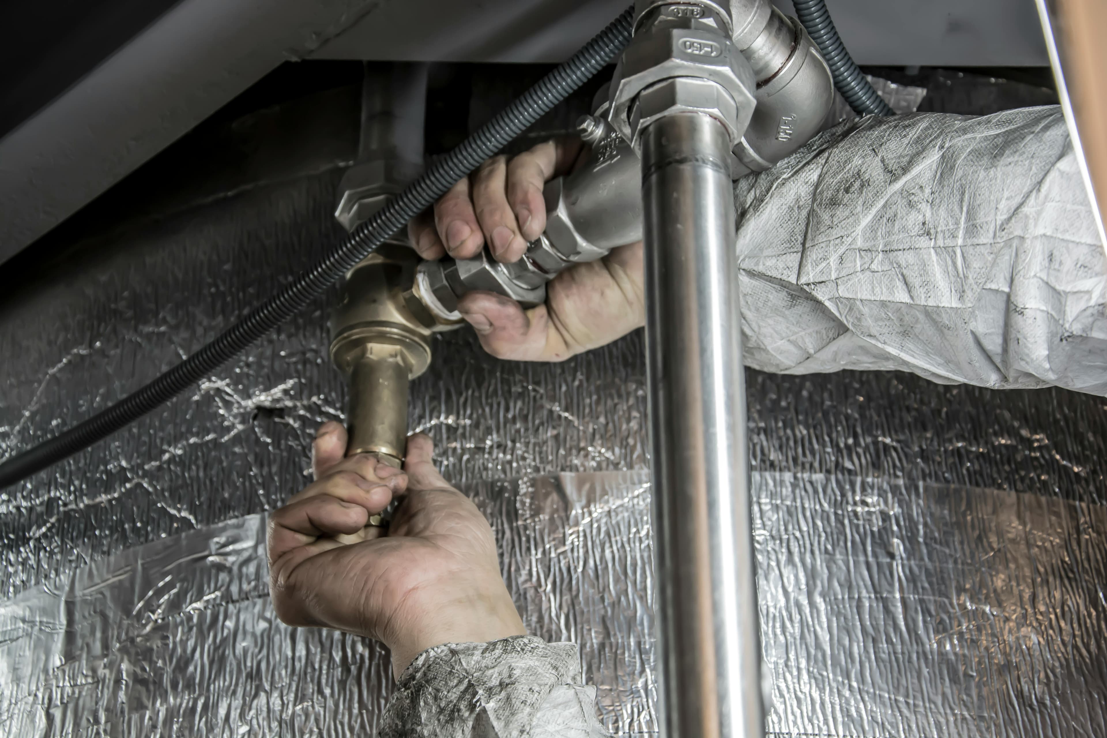 Hands in a white protective suit tightening metal pipe fittings against a reflective foil background.