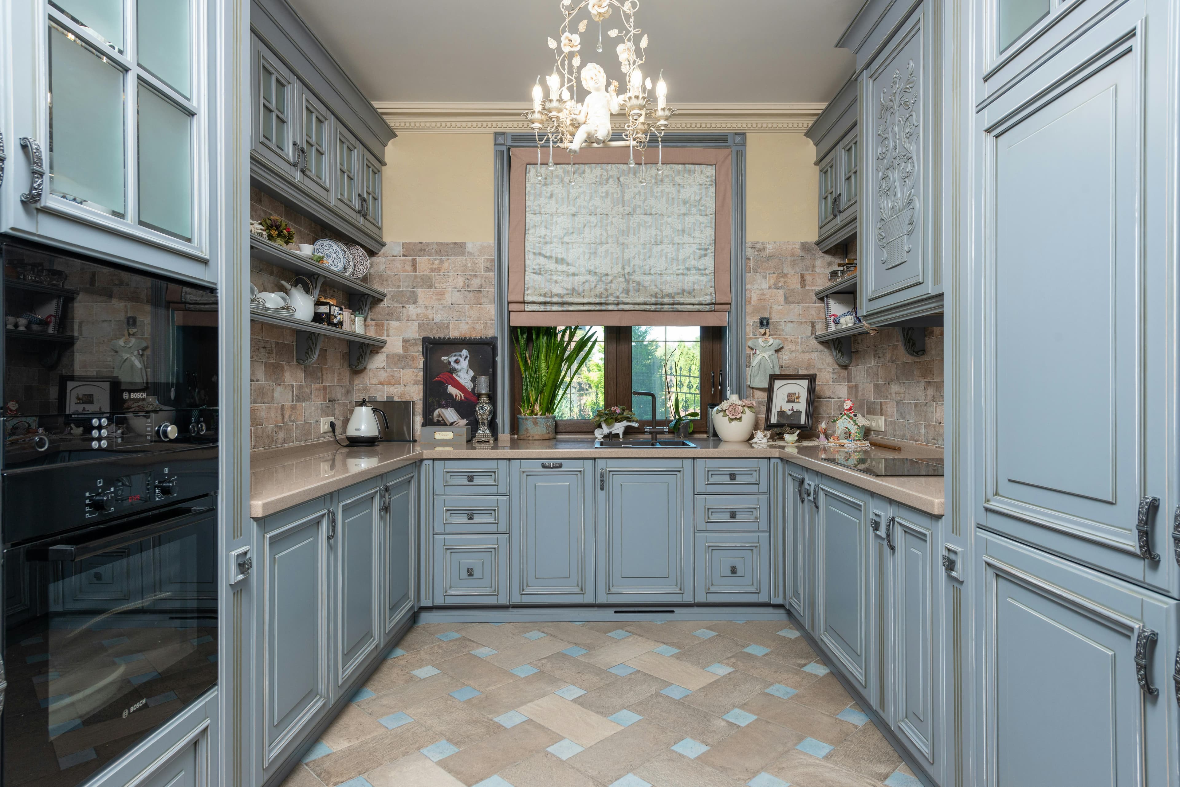 Ornate U-shaped kitchen with light blue cabinets, stone backsplash, and a decorative white chandelier.
