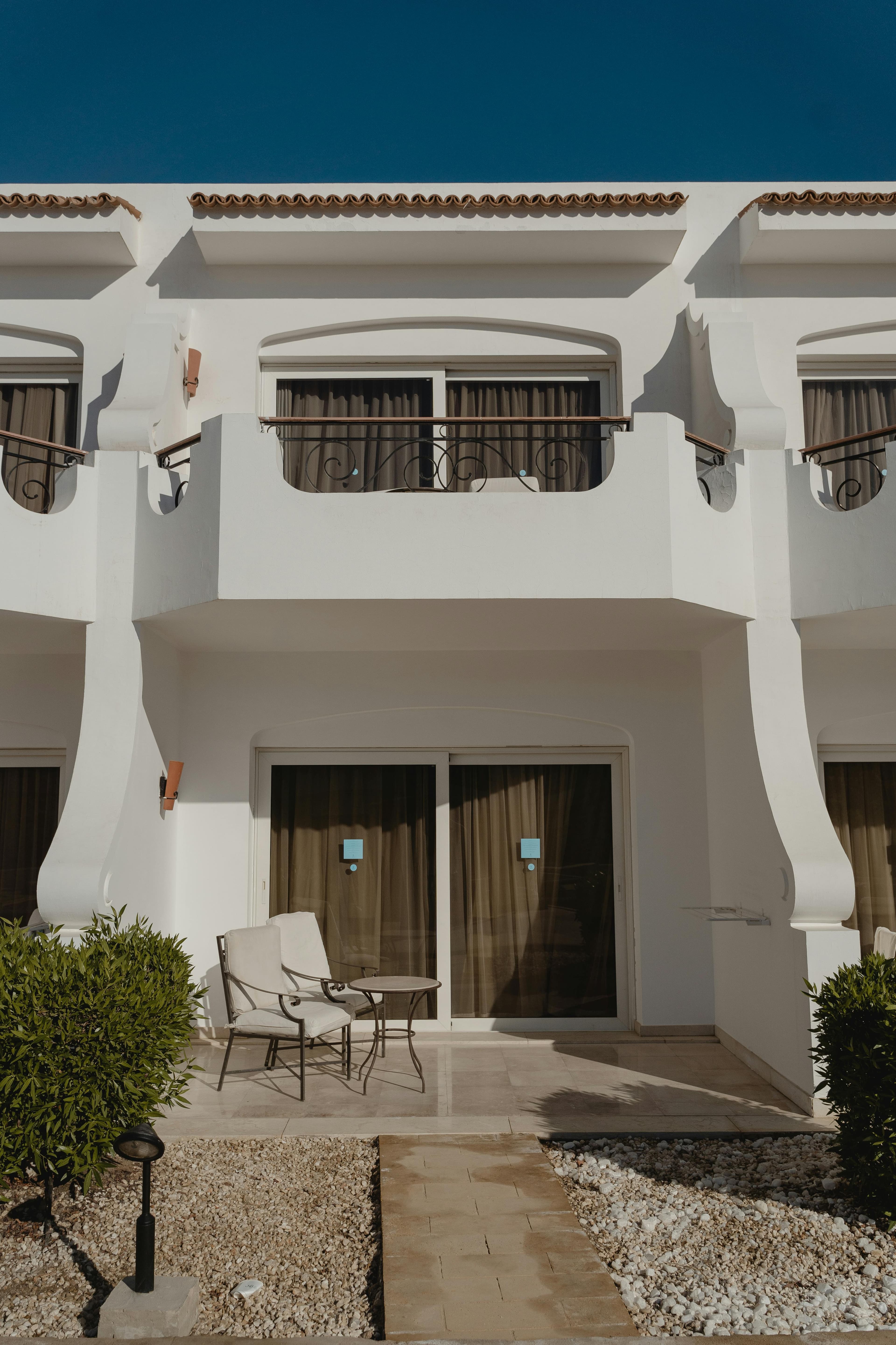 White Mediterranean building with balconies and a ground-floor patio under a clear blue sky.